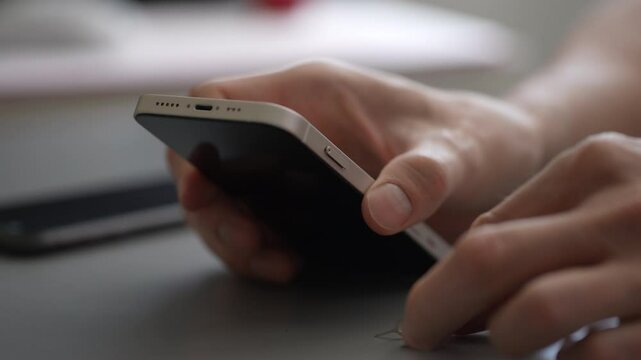 Close-up cropped shot of unrecognizable man skillfully removing SIM card from smartphone using metal eject tool, illustrating process of changing or replacing sim for better connectivity, slow motion.