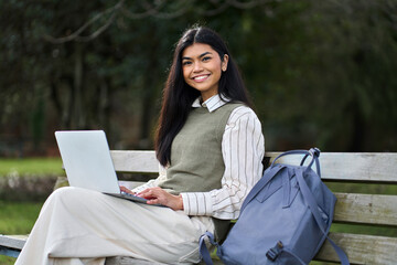 Portrait of happy pretty Asian teen girl college student on bench in nature park using computer...