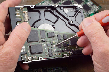 In this photo, the hands of an old craftsman perform repairs and maintenance on the electronic...