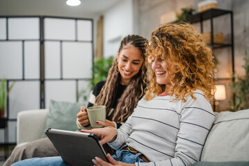 cheerful female friends sit on sofa and enjoy while use digital tablet