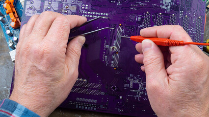 This photo shows the hands of an old electronics repairman diagnosing and repairing computer...