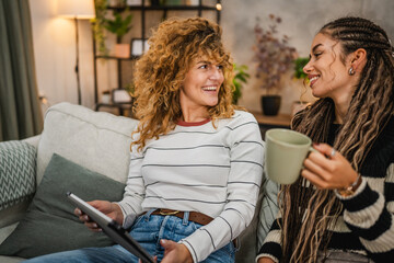 cheerful female friends sit on sofa and enjoy while use digital tablet