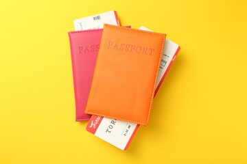Passports in color covers and flight tickets on yellow background, top view