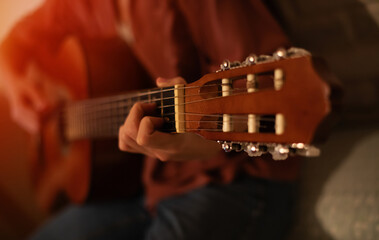 A close-up of a person's hand strumming a classical guitar, showing the fretboard and tuning pegs....