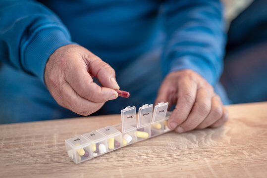 Senior man taking medication from pill organizer at home - Powered by Adobe