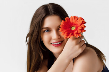 Smiling young woman in blue top holds red gerbera daisy on white background, ideal for International Women's Day or Mother's Day celebrations.
