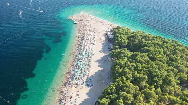 Aerial view of Zlatni Rat beach in Bol, Croatia, during peak summer. The video captures the entire beach, famous for its unique shape, clear waters, and vibrant summer atmosphere.