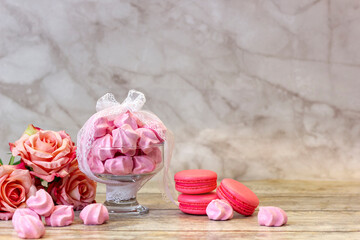 macarons and pink meringue in a vase with ribbon and beads on a wooden background close-up, space for text