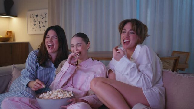 Joyful women watching movie eating popcorn at dark apartment couch closeup. 
