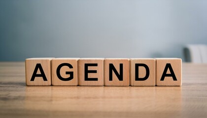 英単語のAGENDAの文字が書かれた木製のキューブブロックが横に並んでいる。aiで生成	

