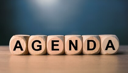 英単語のAGENDAの文字が書かれた木製のキューブブロックが横に並んでいる。aiで生成	
