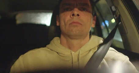 A driver is shown in a vehicle at night, wearing a serious expression and focused on the road
