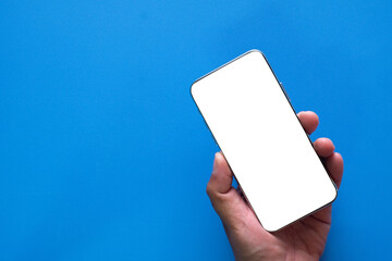 Blank white screen smartphone in hand over blue background with copyspace for put text or logo.,idea for mockups, mobile app presentation,technology themes, digital advertising.