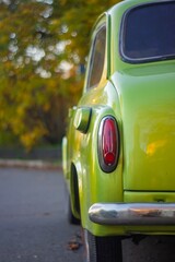 Fototapeta premium A bright yellow vintage British car with rounded body is parked outdoors in a suburban or park setting, likely late afternoon