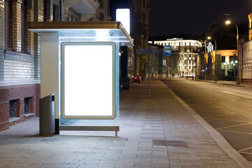 Empty billboard at the bus stop, night city lights. Quiet street without people. Mock-up.