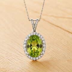 A silver necklace with a round green gemstone pendant and a halo of smaller diamonds.