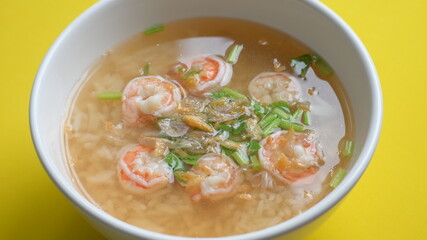 rice soup with shrimp in white bowl on yellow background