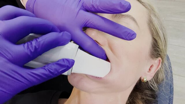 Orthodontic office, doctor scanning teeth with a handheld wand/intraoral scanner before Invisalign treatment.