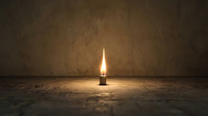 Single candle flame burning brightly on rustic wood floor against textured wall, hope, remembrance