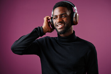Young Black man with headphones enjoying music, smiling against a purple background, showcasing...