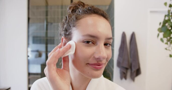 Applying facial toner with cotton pad, woman enjoying skincare routine at home