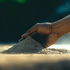 Human hand gently touching sand on a beach during sunset