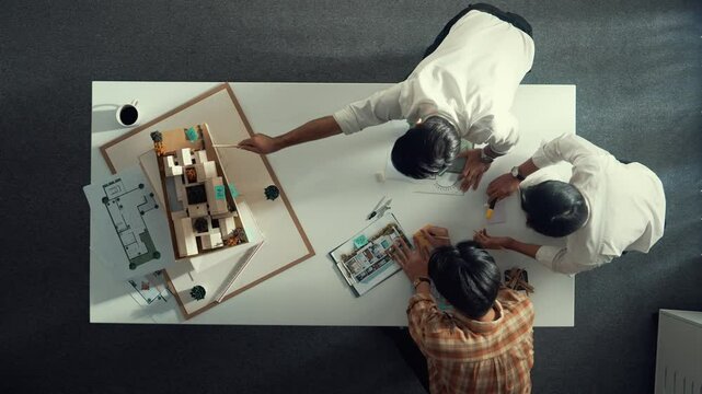 Group of skilled designer looking at model while discussing about building. Top view of architect engineer explain idea while talking and writing blue print scattering at meeting table. Alimentation.