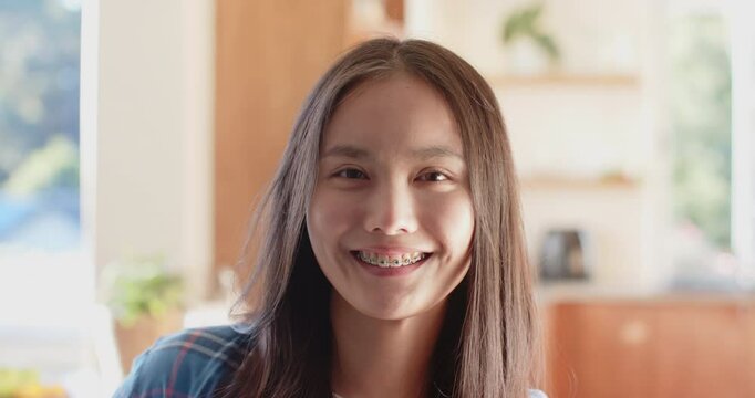 Smiling asian teenage girl with braces looking at camera in bright indoor setting, copy space