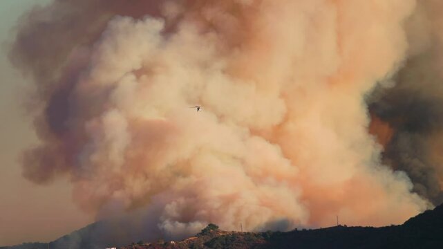 Dramatic and intense scene of wildfire in Los Angeles, showcasing thick smoke, helicopters hovering above, and ongoing rescue efforts amidst the widespread destruction in the mountains, California