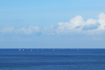 Sailboats Glide Across Blue Ocean Under a Cloudy Sky on a Sunny Day