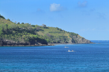 Tranquil Ocean Meets Lush Coastline: Boats Sail Across Blue Water with Scenic Cliffside Views of Nature and Tropical Paradise.