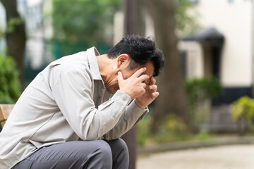 ベンチを座りながら落ち込んでいるミドル男性　ライフスタイルイメージ