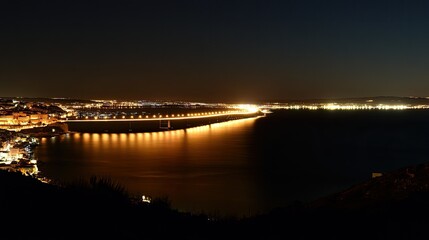 Naklejka premium Nighttime panorama of the Vasco da Gama Bridge, with golden lights reflecting in the water and Lisbon's cityscape in the distance