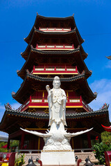 Fototapeta premium A detailed close-up of a magnificent white Guan Yin statue, positioned in front of a vibrant red and gold Chinese pagoda.