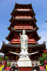 Obraz premium A detailed close-up of a magnificent white Guan Yin statue, positioned in front of a vibrant red and gold Chinese pagoda.