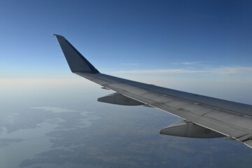 Fototapeta premium Aircraft wing flying over landscape with large lake, copy space.