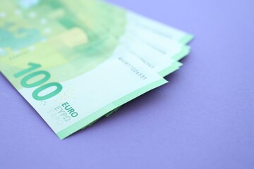 Big amount of one hundred euro money bills on lilac background