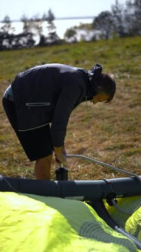 A man in wetsuit pumps up a kiteboarding kite on a beach