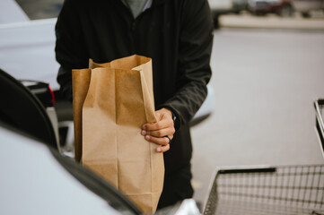 Close up of hands placing paper grocery bag into car trunk outdoors