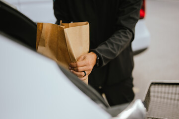 Close-up of man's hands placing a paper grocery bag into a car trunk