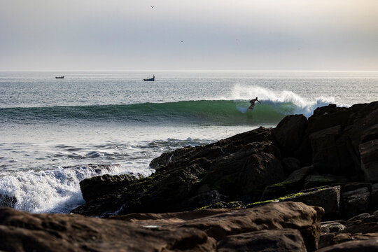 Male surfer rides waves with rocky foreground - Powered by Adobe