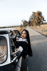 a girl with long dark hair looking out of a car window. She is wearing a black jacket with white...
