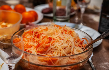 Salad with funchosa in a glass salad bowl close-up on the background of dishes on the table