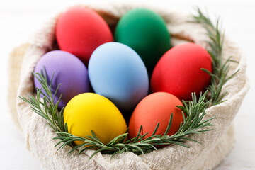 Colorful Easter eggs in a basket on white wooden table.