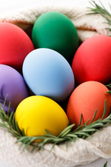 Colorful Easter eggs in a basket on white wooden table.