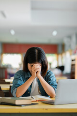 Student Deep in Thought at Library Desk with Open Books and Laptop in Bright Study Environment