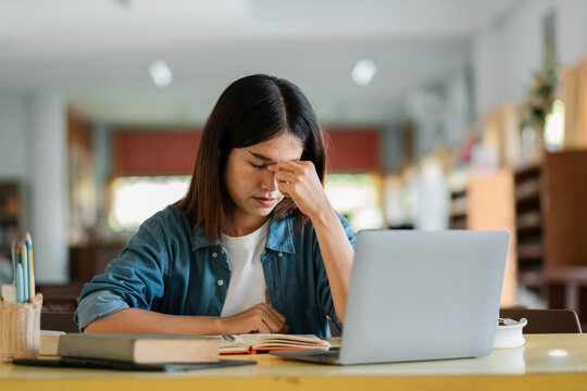 Young Woman Stressed While Studying with Laptop in Library, Overwhelmed Student Preparing for Exams, Academic Pressure and Mental Health