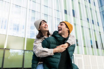 Happy couple laughing together outdoors in urban setting, piggyback ride