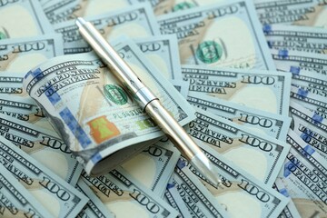 Golden pen clipping big amount of hundred dollar bills US banknotes