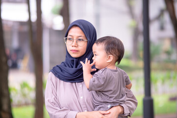 Fototapeta premium image of an asian mother and baby having fun in the park. Mother and baby playing in the park at the sunset time. Family, trust, protecting, care, parenting, summer vacation concept.